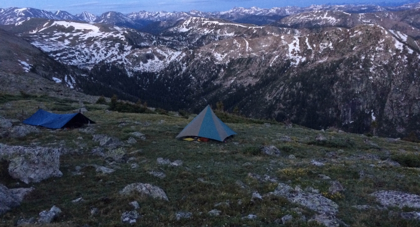 tents and shelters are set up high above a vast mountain landscape